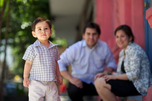 A toddler boy walks near his parents.
