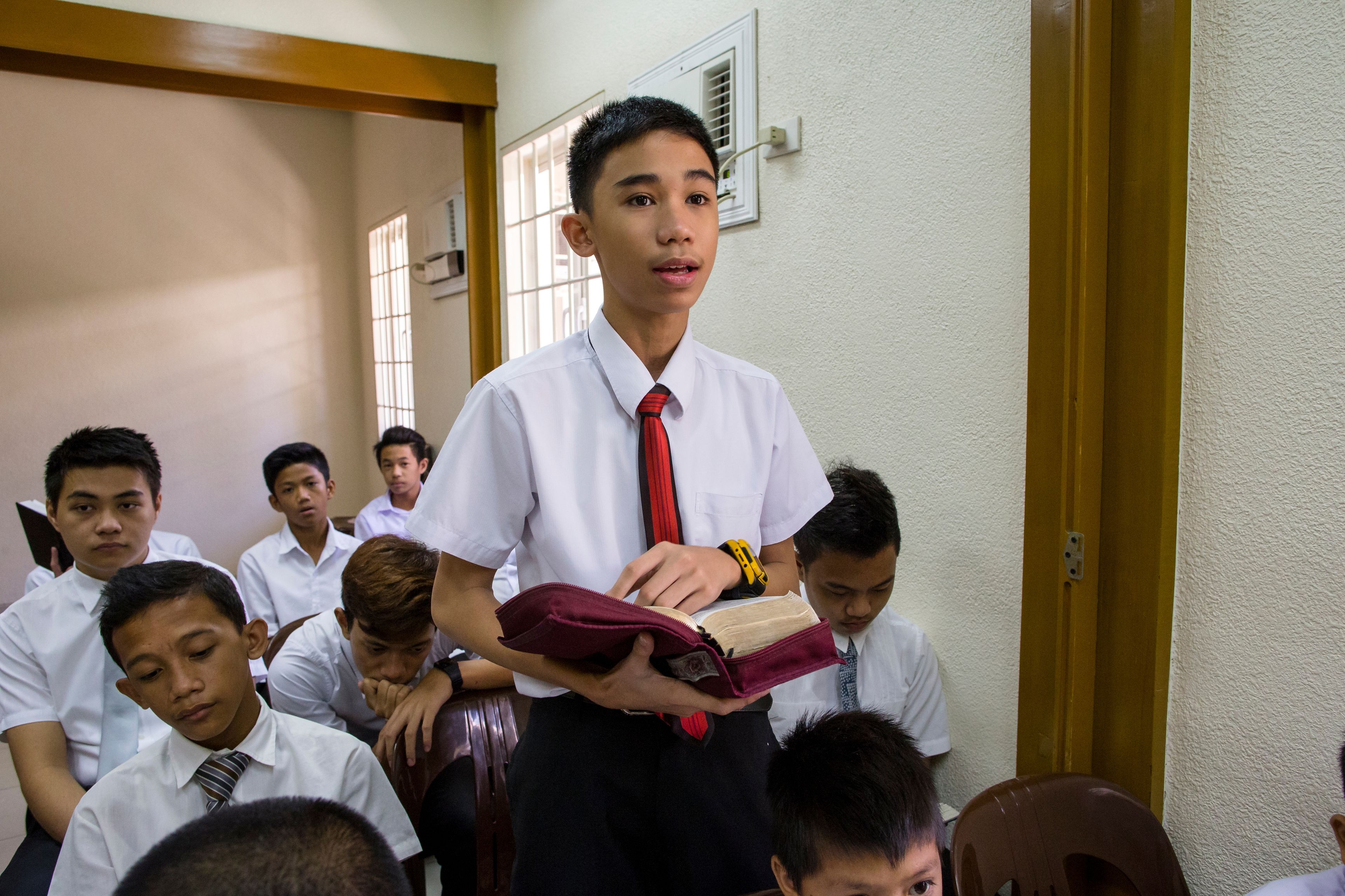 A young man stands up during priesthood meeting and reads from his scriptures.  