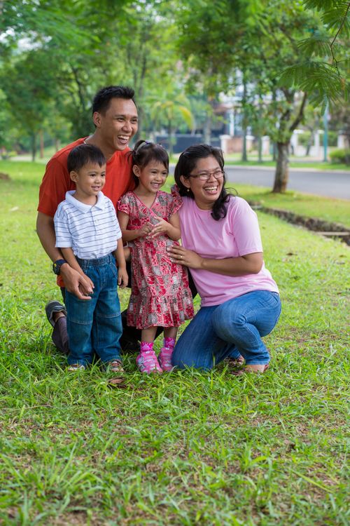 A mother and father stand on the grass and smile with their two children.