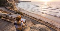 A young adult male sits on a rock at the edge of a cliff. He is reading the scriptures as the sun begins to set.