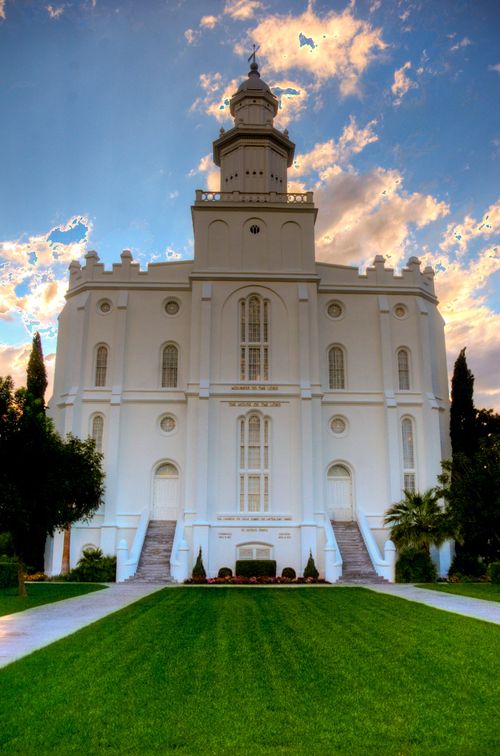 The front of the St. George Utah Temple, with a view of the grass leading up to the front and staircases leading up to the doors.