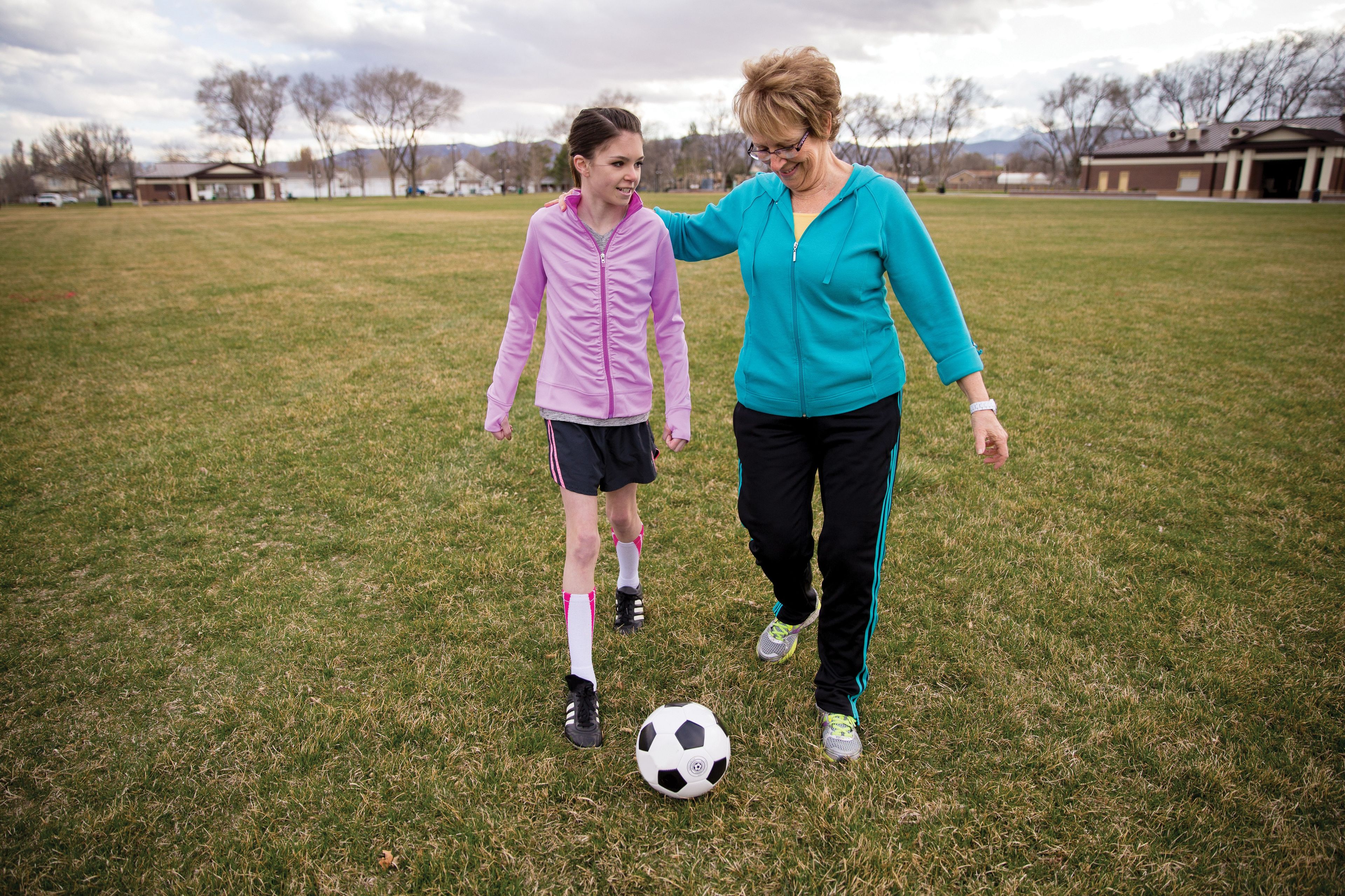 A grandmother plays soccer with her granddaughter in a large field.