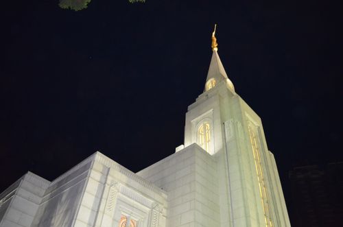 The Curitiba Brazil Temple spire lit up at night against the black sky.