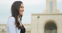 Young adult woman stands smiling in front of a temple.