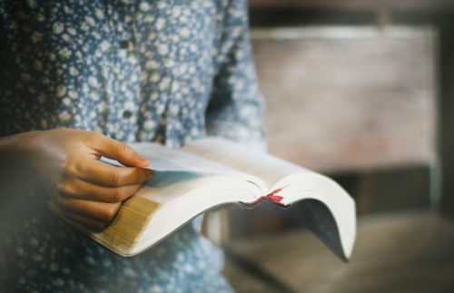 young adult holding an open Bible