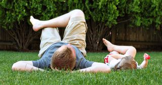 a father and child lie on the grass