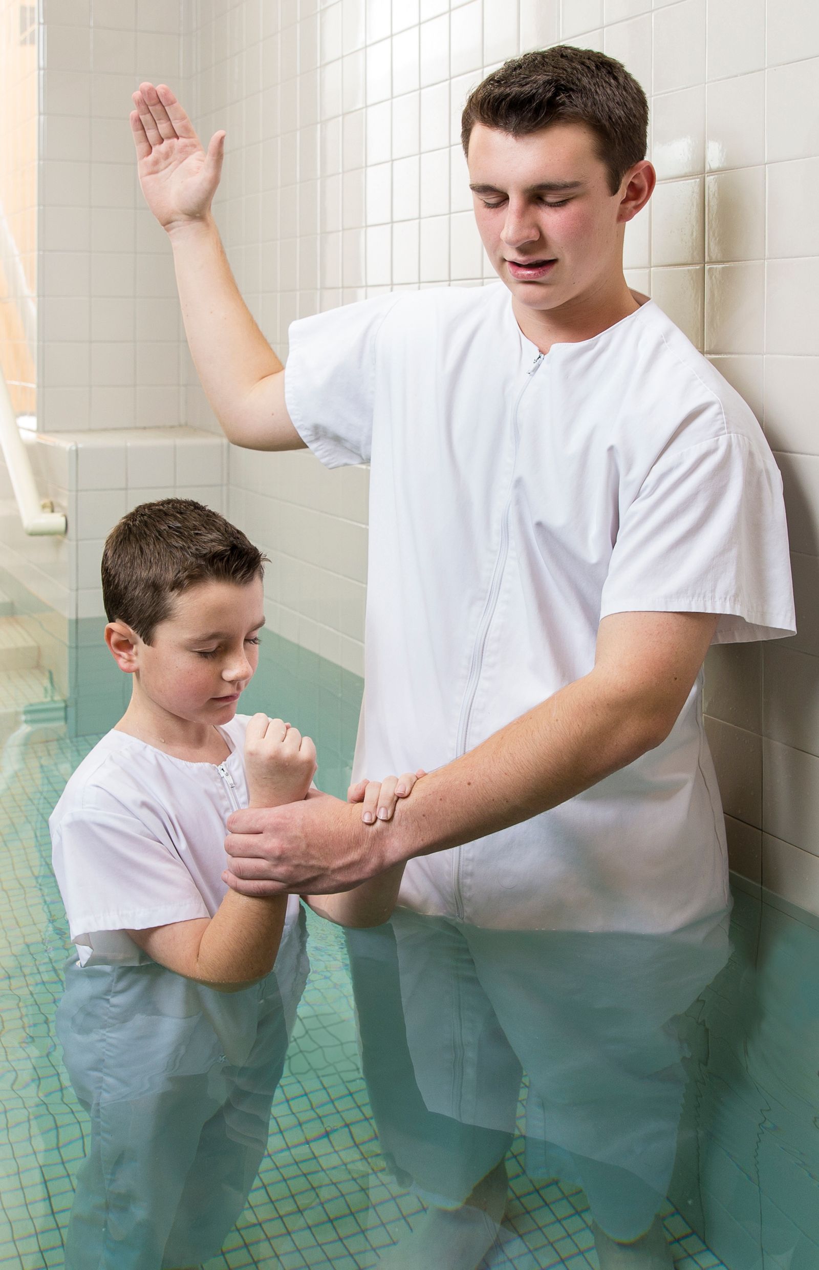 A young man baptizing a boy in a baptismal font.