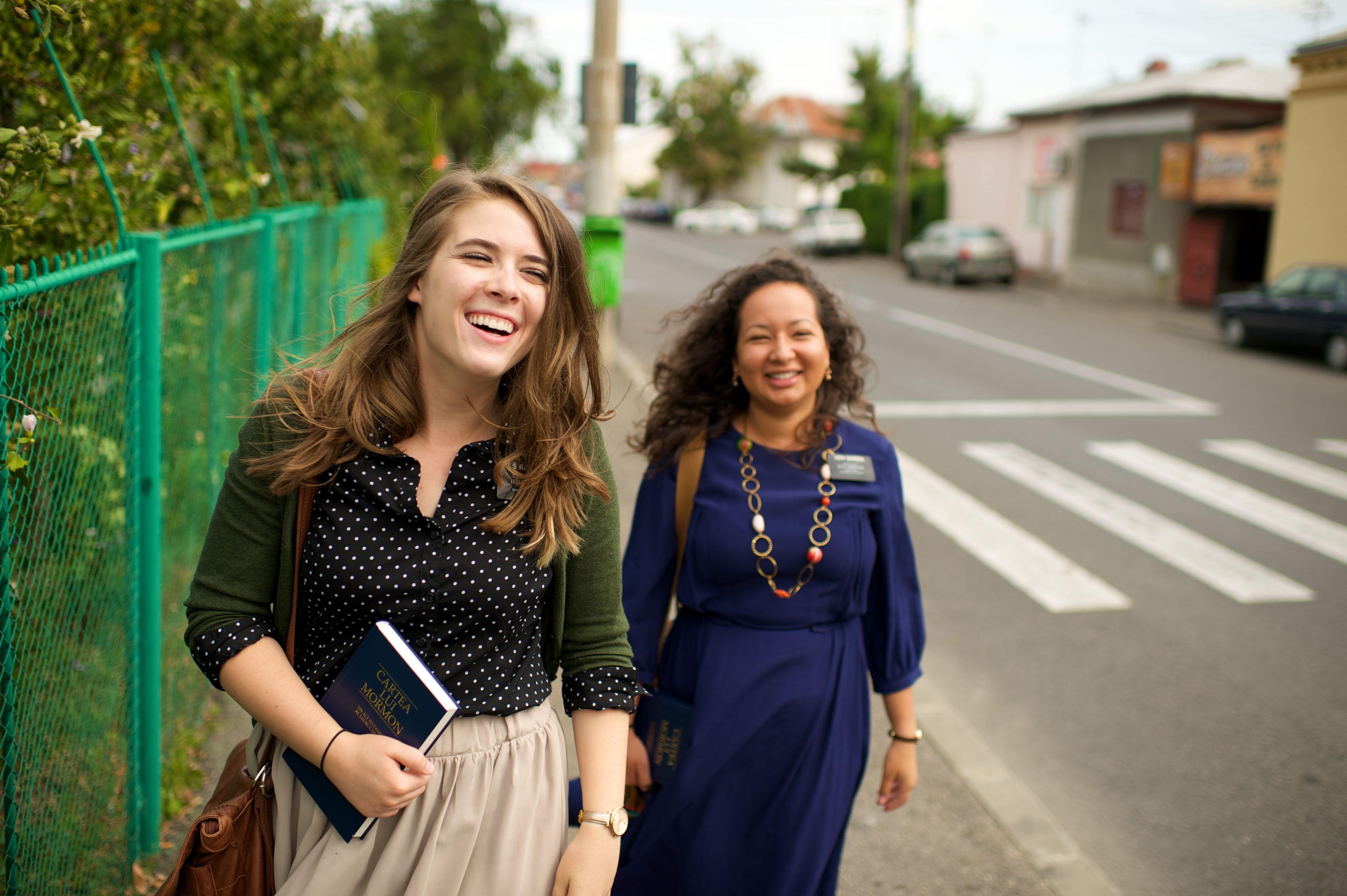 Two sister missionaries in Romania laugh while walking down a street together.