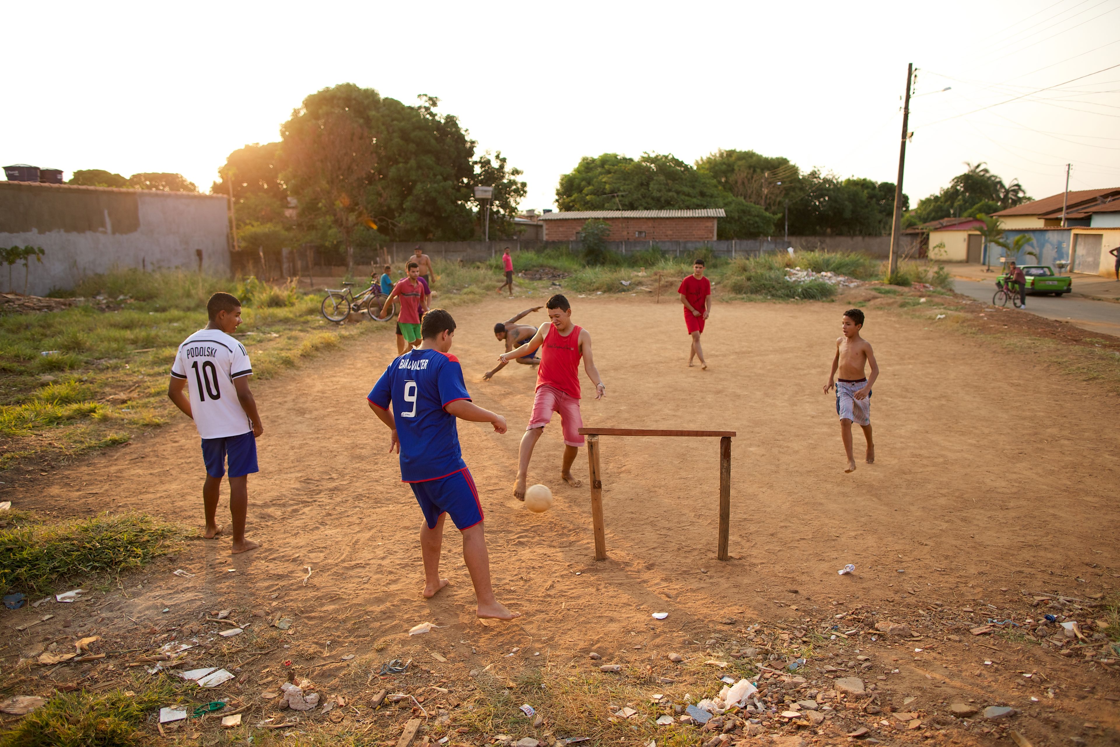 Young men in Brazil play soccer on a dirt field.