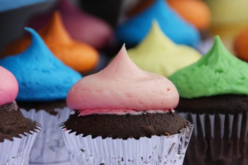 Chocolate cupcakes in gray cupcake papers, each with a bright-colored frosting.