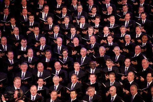 A section of the men from the Mormon Tabernacle Choir in black suits and purple ties, singing from the music they hold in their hands.