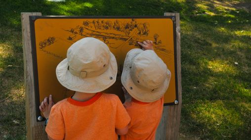 Two young boys in orange shirts and hats pointing at figures on a map. 