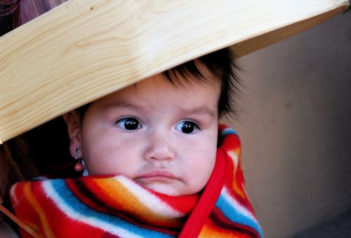 A baby girl with earrings is wrapped in a striped blanket.