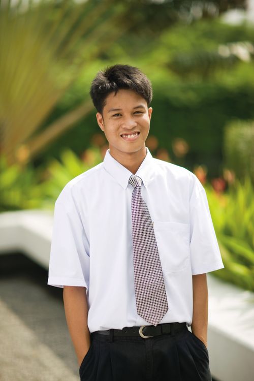 An outdoor portrait of a young man from the Philippines wearing a white shirt, black pants, and a red and white checkered tie.