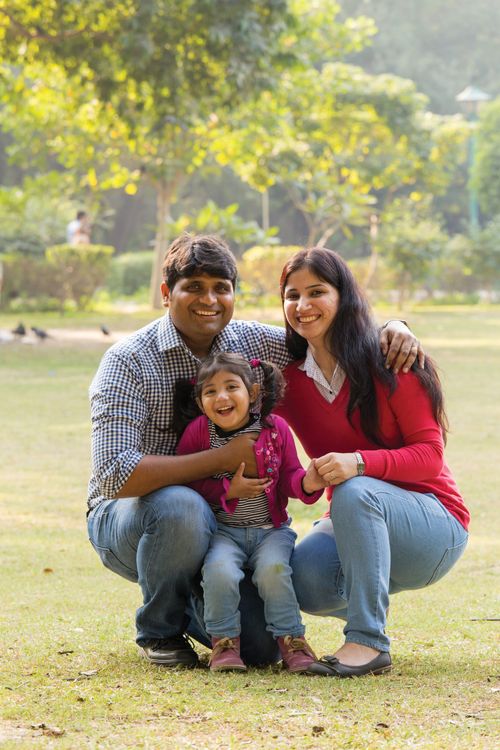 A husband and wife in the park with their toddler-age daughter, smiling.