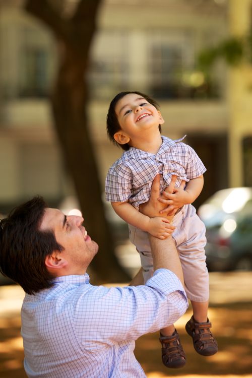A father holds his son up and plays with him outside.