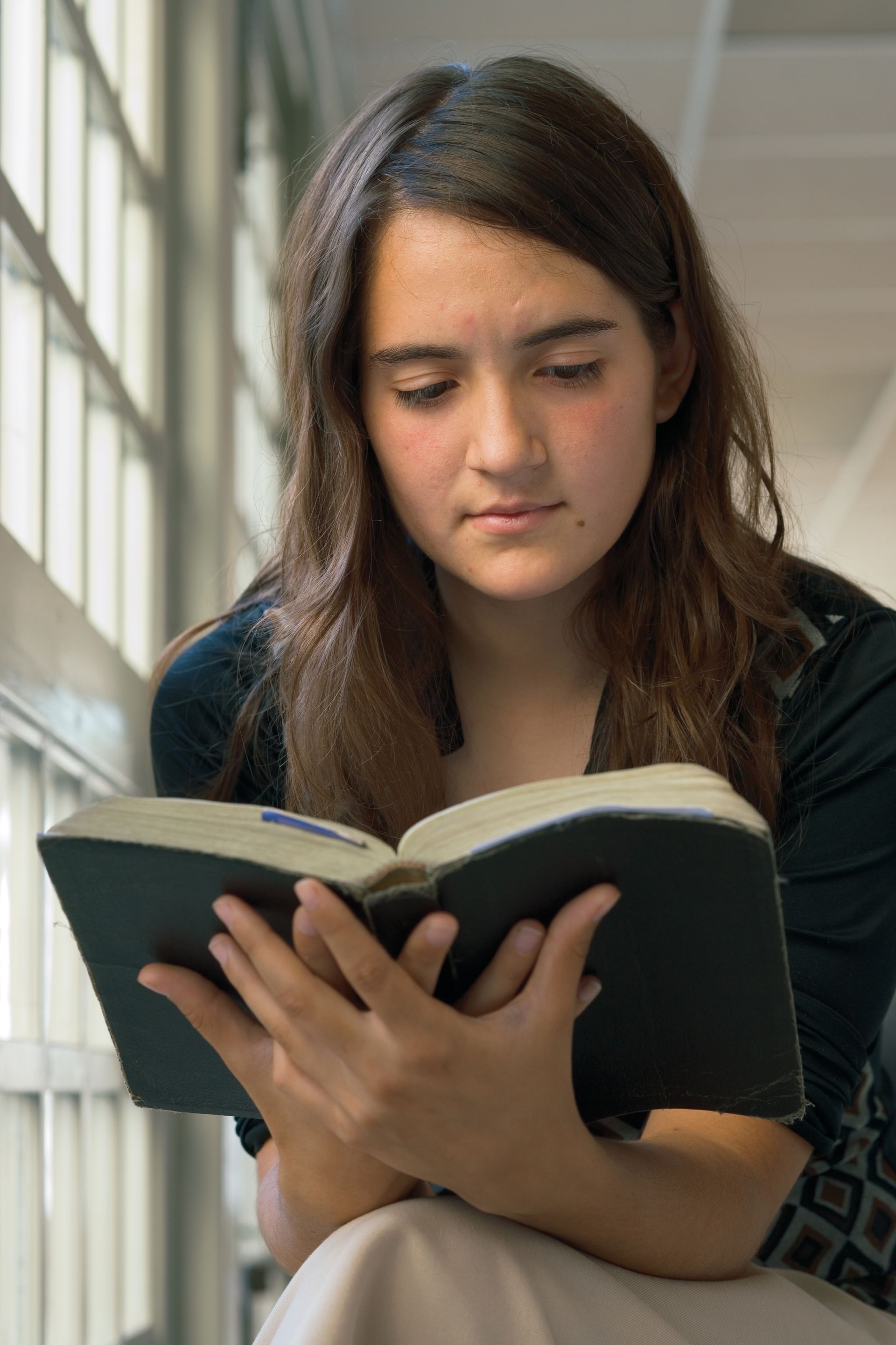 A young woman leans forward to read her scriptures.
