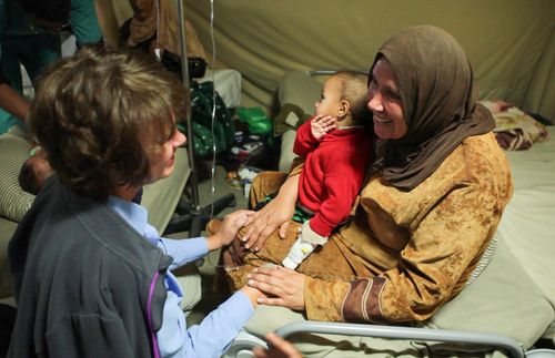 A woman comforts another woman and her child. They are in a refugee camp.