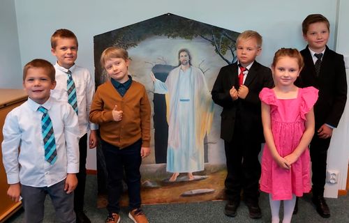 Primary children stand together with an illustration of Jesus Christ in Kuopio, Finland.