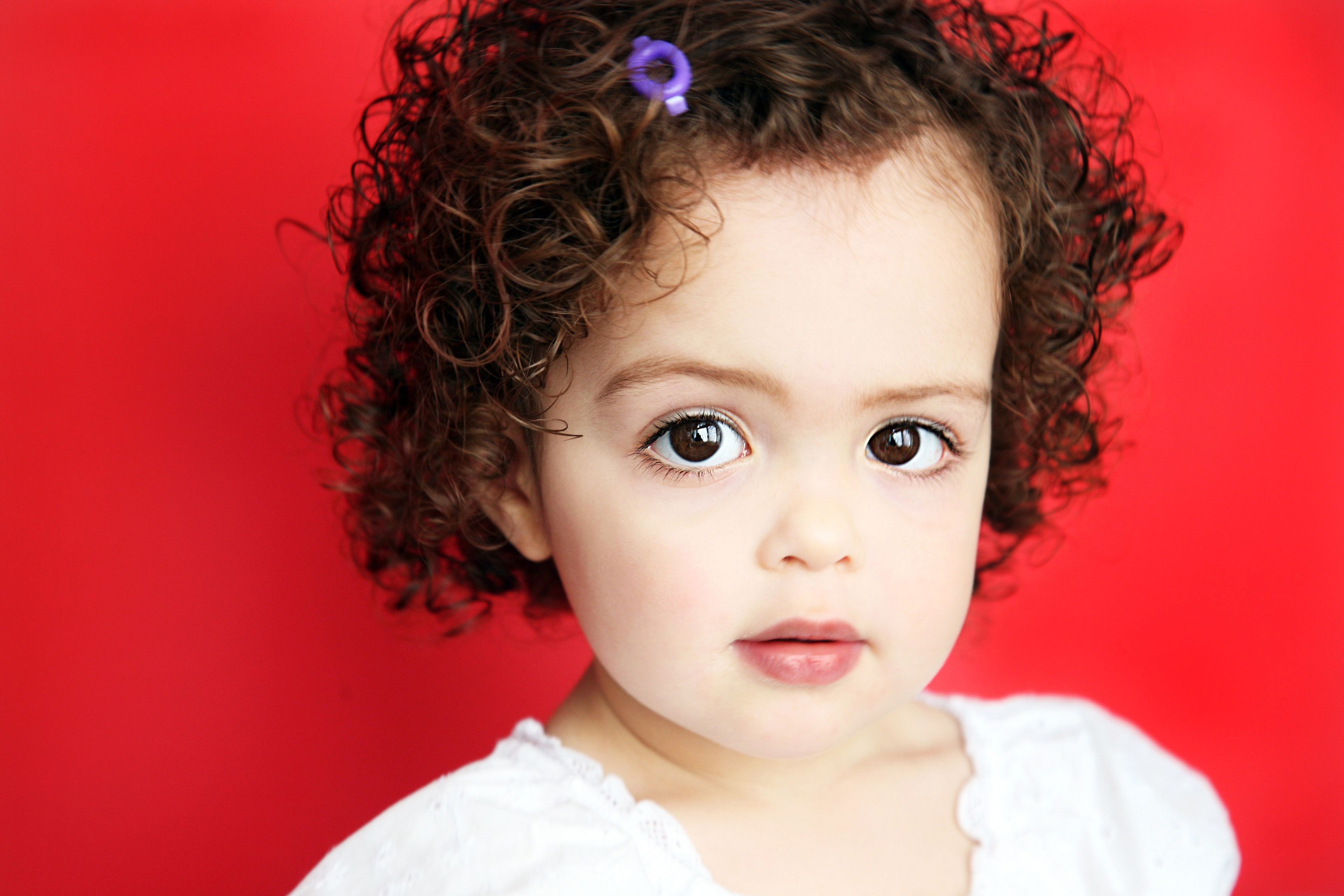 A portrait of a toddler girl with a red background.
