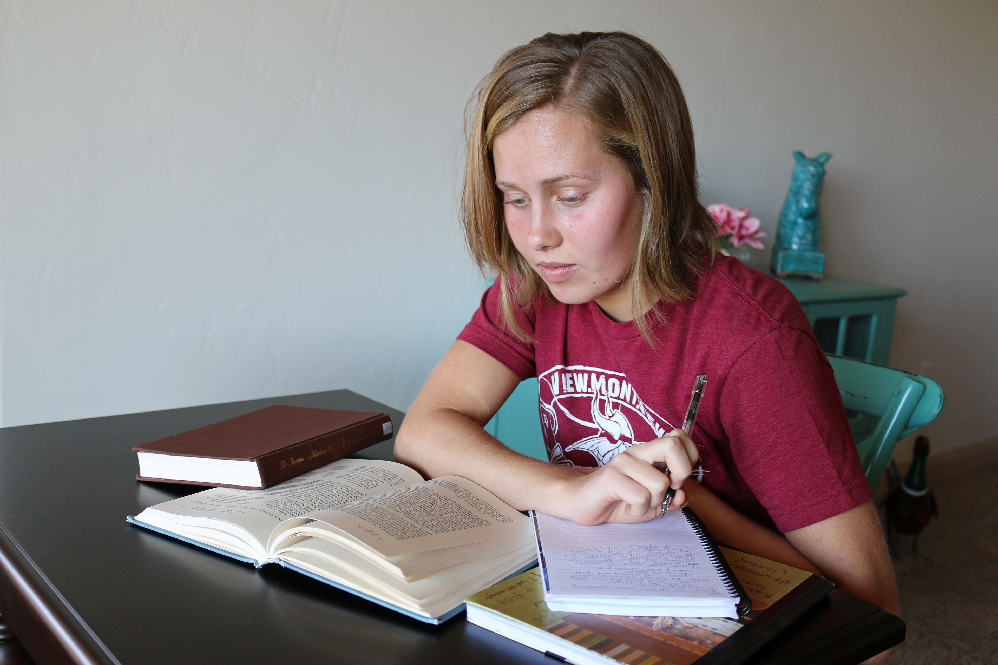 A young woman sits at a desk and studies the scriptures.