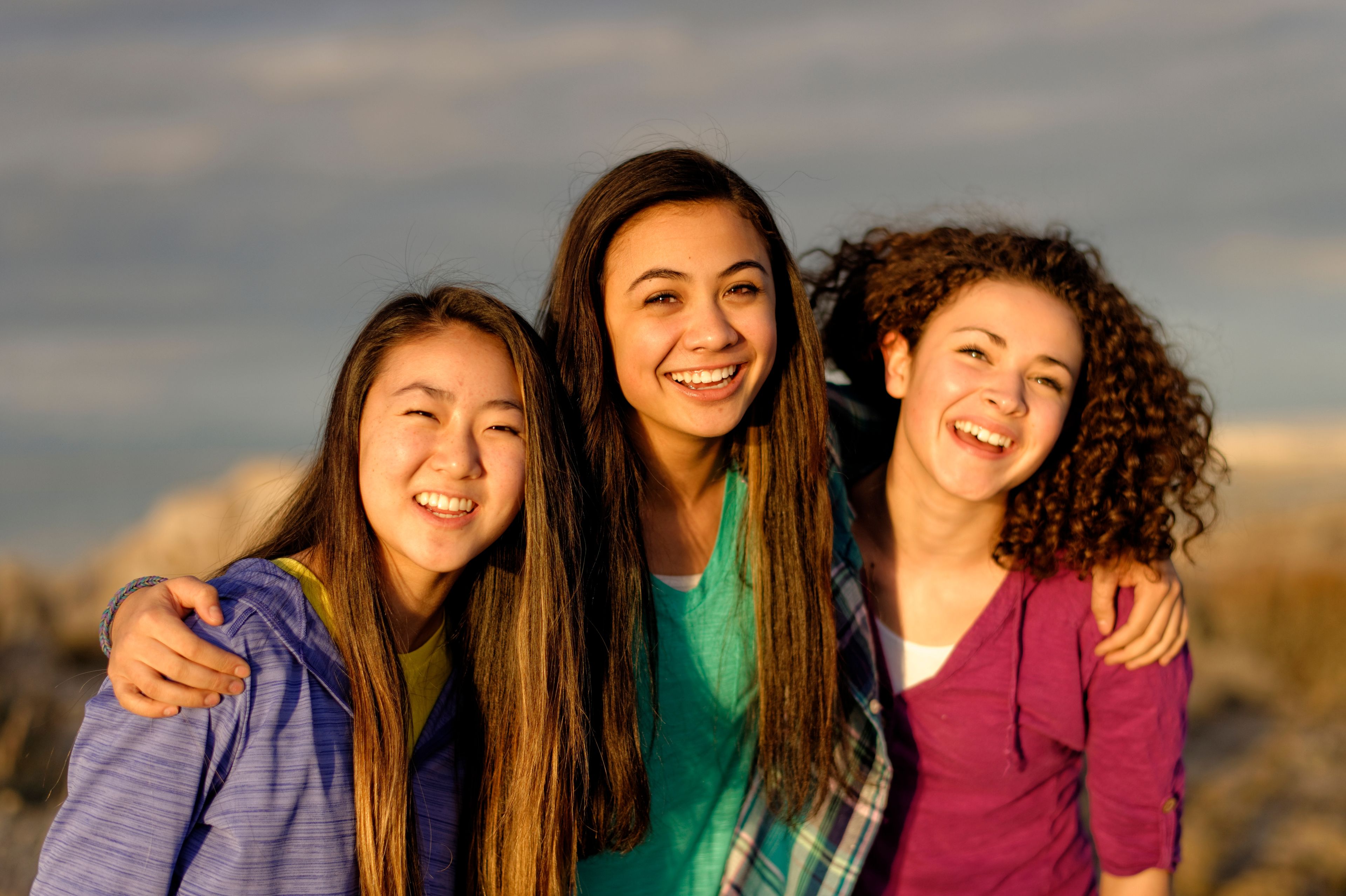 Three young women stand together and smile while enjoying a hike or nature walk.