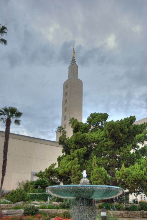 A water fountain on the grounds of the Los Angeles California Temple, with a green tree and the temple’s spire in the distance.