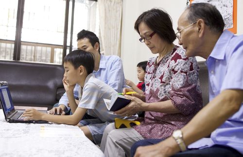 Family group in Taiwan sitting together looking at a computer, talking and looking at photographs.