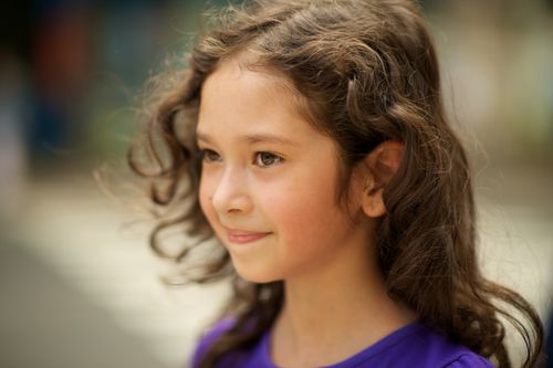 A side profile of a young girl from Argentina with wavy brown hair and brown eyes, wearing a purple T-shirt.