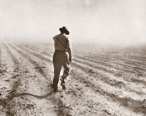 Ezra Taft Benson walking and inspecting a field during a drought, wearing a hat, a long-sleeved shirt, pants, and boots.