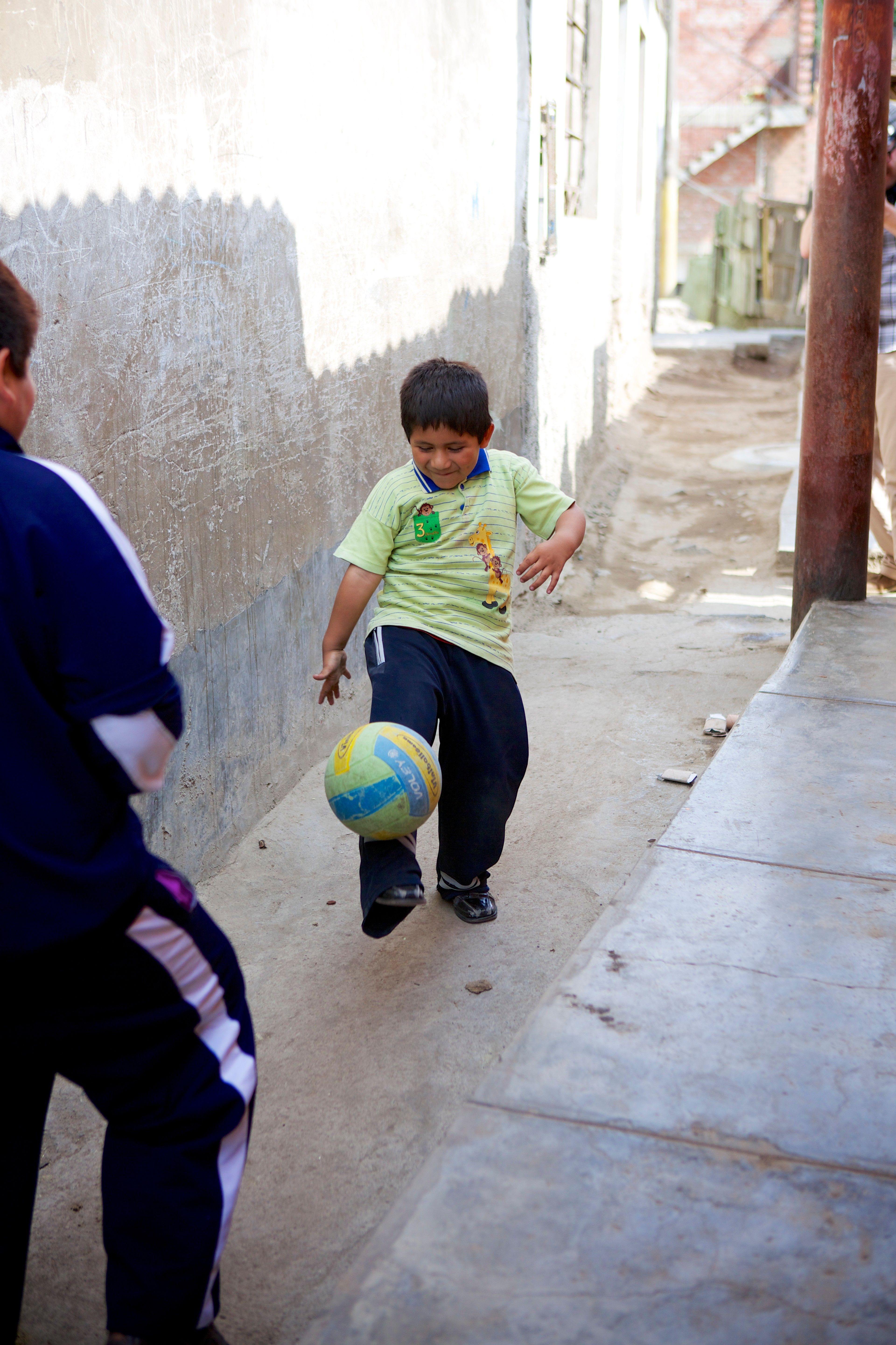 Two Peruvian boys play soccer together in an alleyway.  