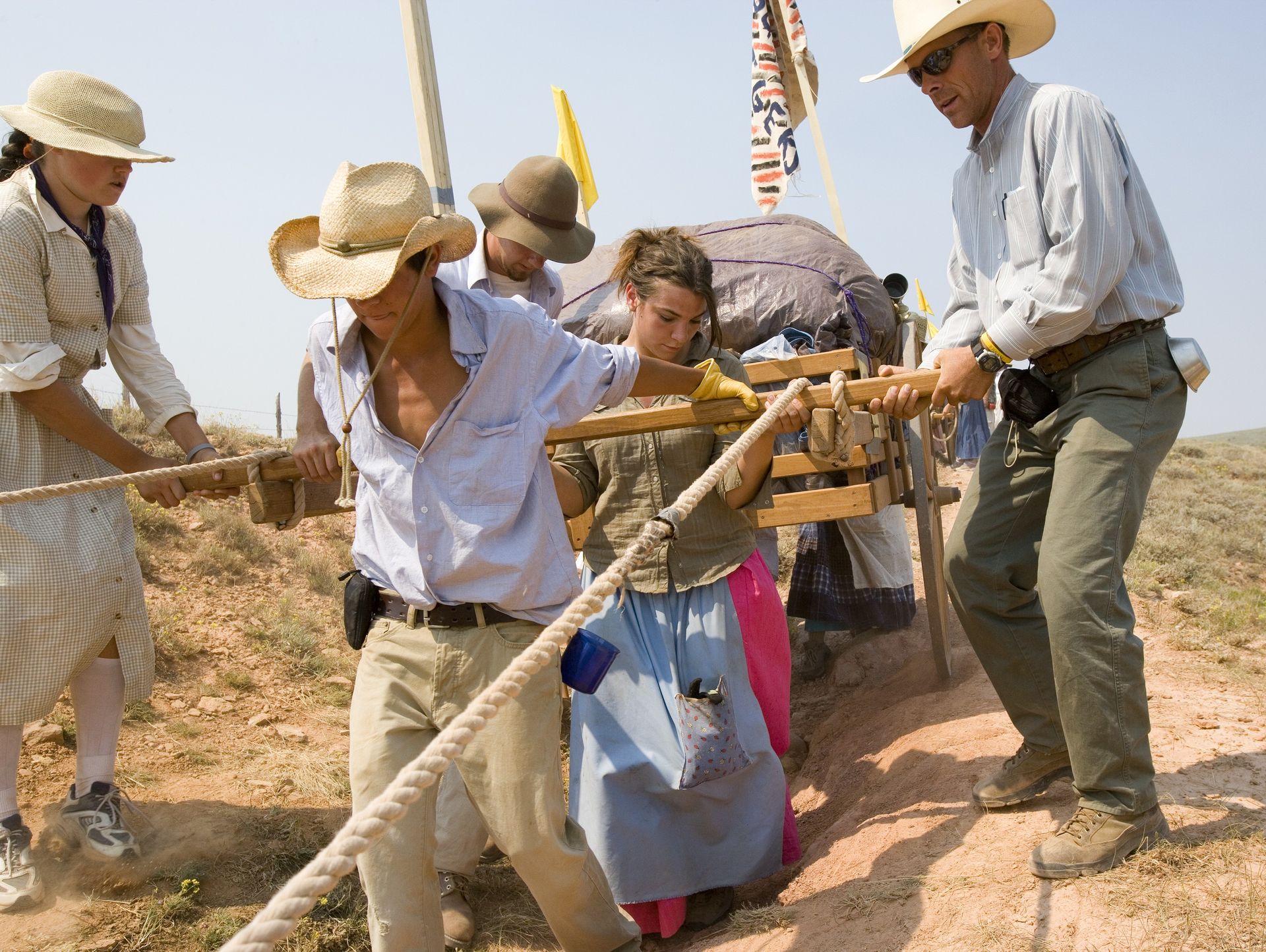 Two young men and one young woman pull a handcart carefully over a rocky and jagged path.