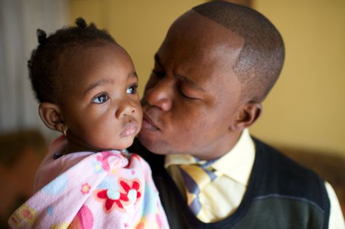 A father in the Congo kisses his infant daughter on the cheek while she stares off into the distance with a serious expression.