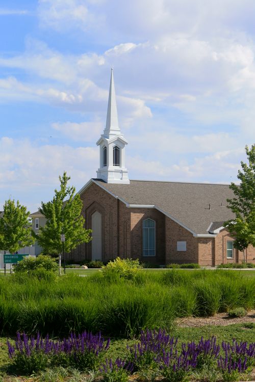 Exterior of LDS Meetinghouse with steeple.  Purple flower beds and ornamental grasses are in land by building. (vert)