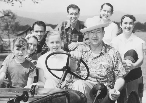 President Benson wearing a hat, sitting at the steering wheel of a car with his children next to him and behind him.