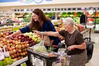 A young adult woman helping an older woman in an electric cart do grocery shopping.