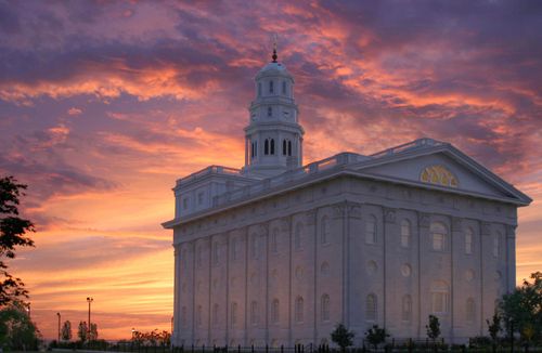 A back and side view of the Nauvoo Illinois Temple in the evening, with an orange and pink sunset filling the sky overhead.