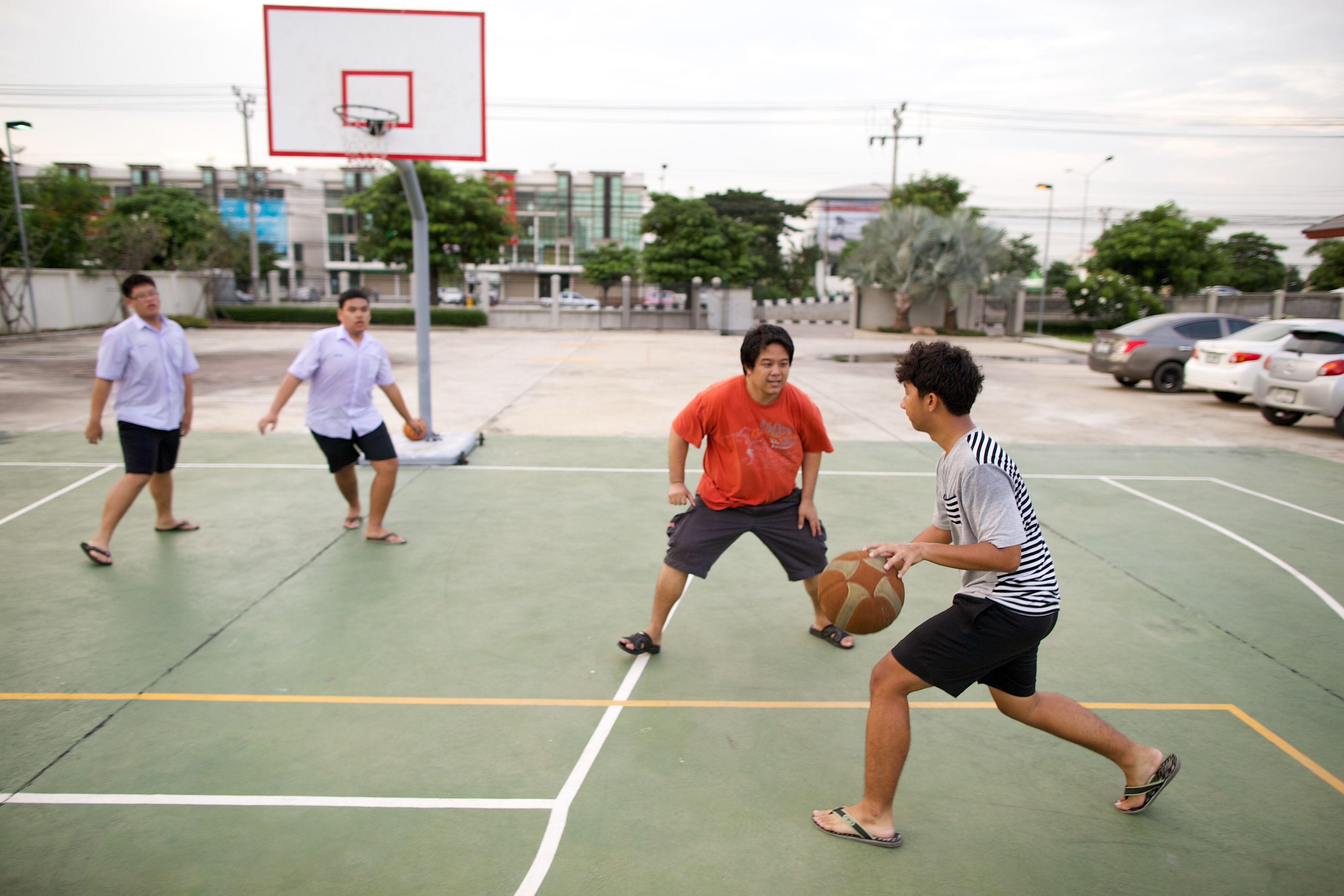 Young men from Thailand play basketball on an outside court.