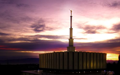 A side view of the Provo Utah Temple lit up, with the sunset in the background.