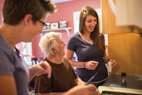 Two young women help an elderly women prepare food in the kitchen.
