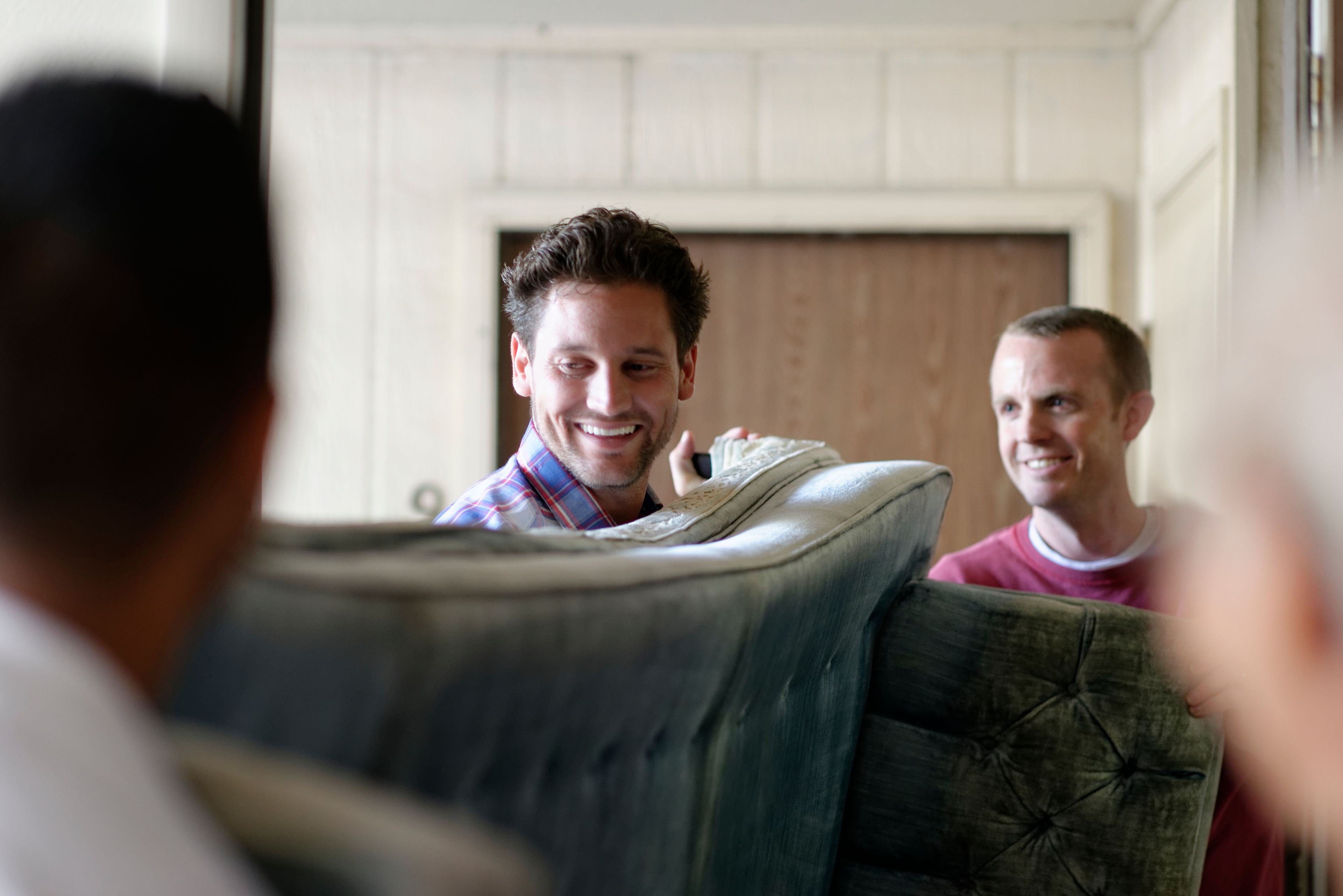 Men help move a couch for an elderly woman.