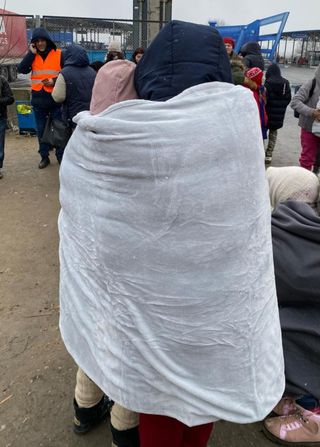 Ukraine Refugees huddle together under a blanket in the rain in Poland