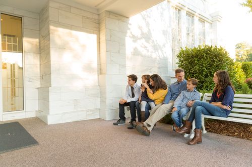 A mother, father, two sons, and two daughters sitting on white benches outside the doors of the Raleigh North Carolina Temple.