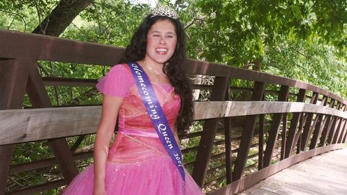 A young woman (Macy Lewis) wearing a pink gown and Homecoming Queen sash.