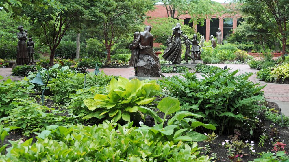 Bronze statues amidst green foliage with a brick building in the background.