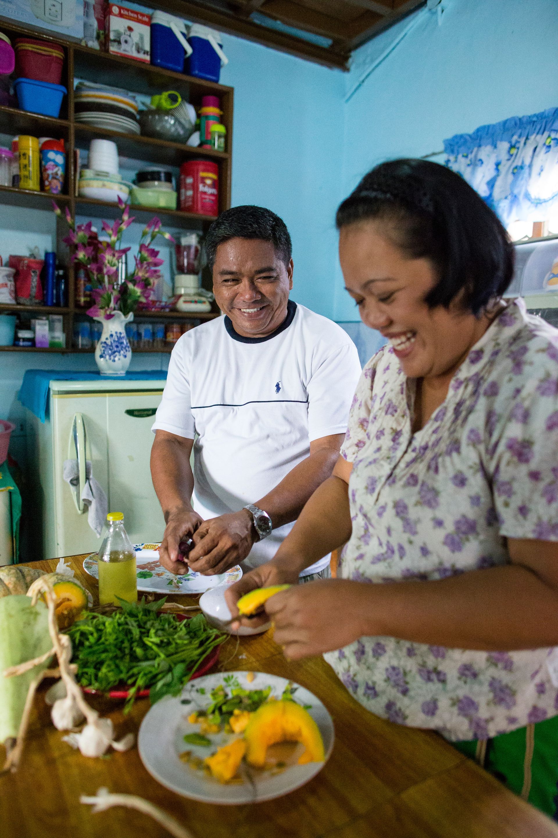 A couple from the Philippines standing in a kitchen and preparing food together.  
