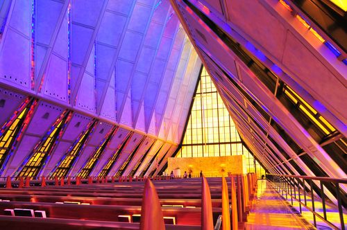 Rows of benches surrounded by stained-glass windows on each side inside a chapel at the Air Force Academy.