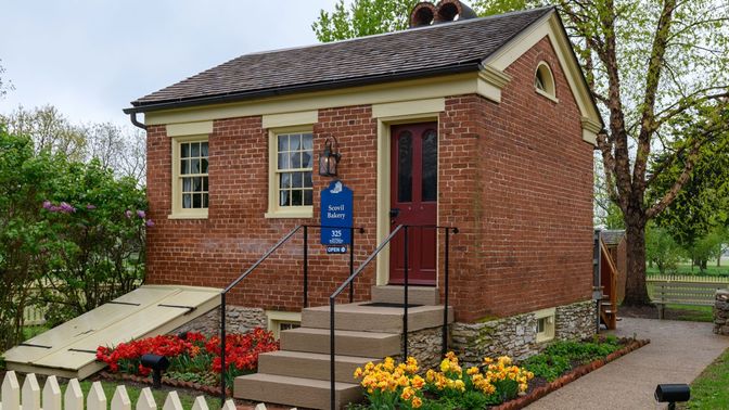 A one-story brick building with stairs leading up to the entrance and a flower garden at the base of the building.