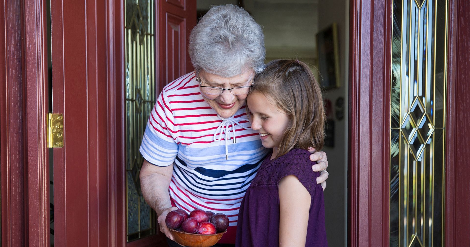 Granddaughter handing her grandmother some freshly picked plums.