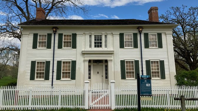 Two-story white house with dark green shutters.